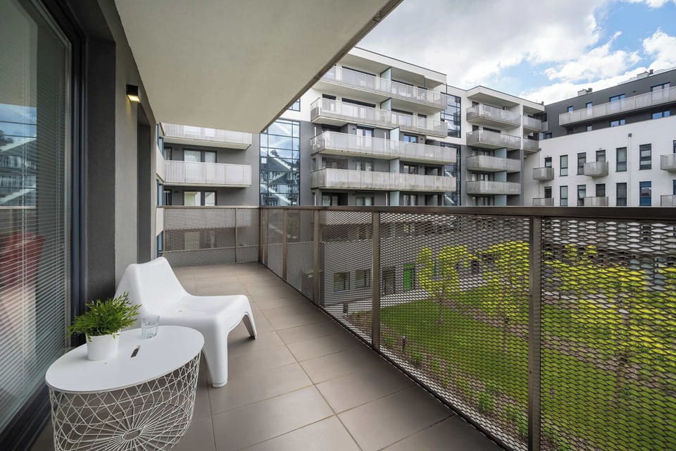 Private balcony with outdoor seating and a pleasant view of the modern residential complex.