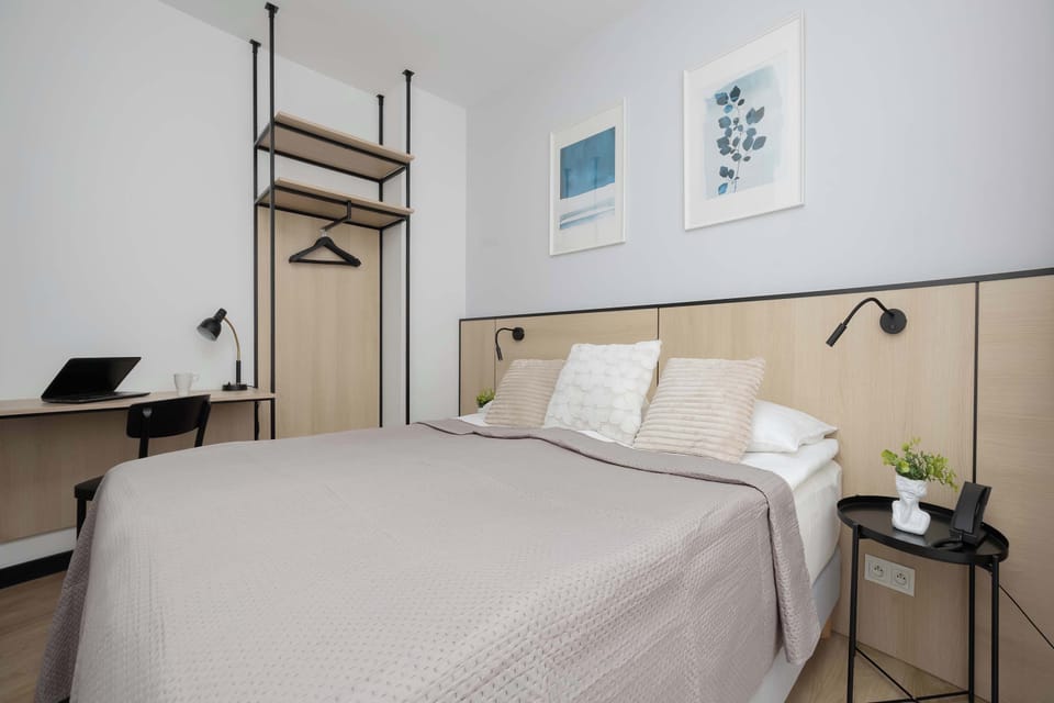 A comfortable bedroom with a large bed, bedside lighting, and framed artwork above the headboard. The room uses beige and gray tones for a relaxing atmosphere.