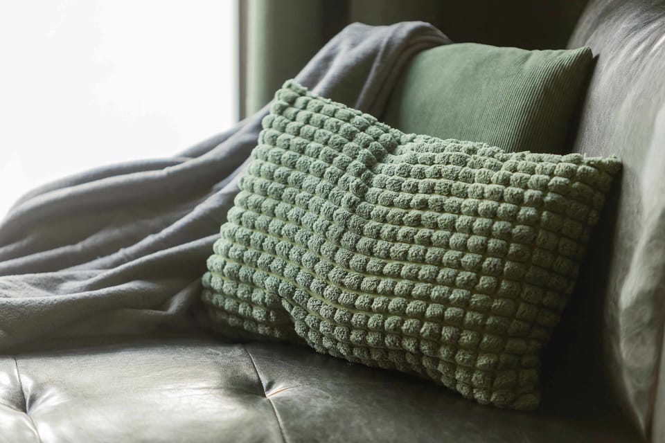 A detailed close-up of a textured green cushion resting on a soft fabric couch. The shallow depth of field emphasizes the fabric patterns.