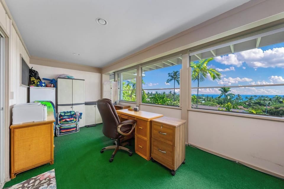 A dedicated workspace with desk and seating overlooks tropical palms and sparkling ocean waters, framed by expansive windows that flood the room with natural island light.