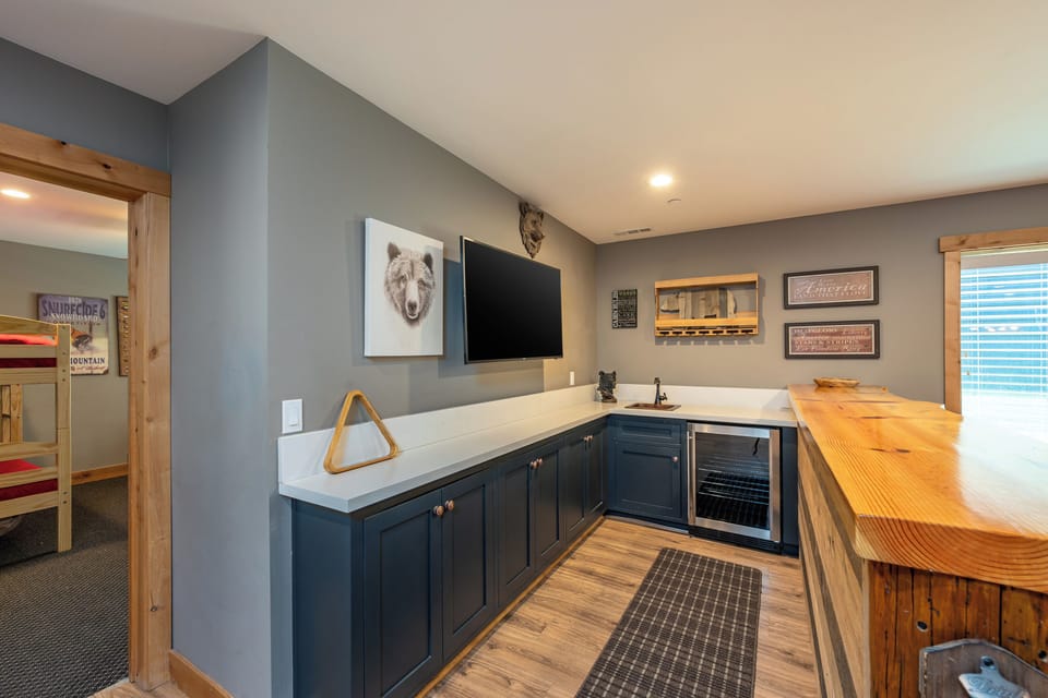 Your entertainment hub features a sleek kitchenette with navy cabinetry, a beverage fridge, and a live-edge bar—perfect for game nights and après-ski cocktails.