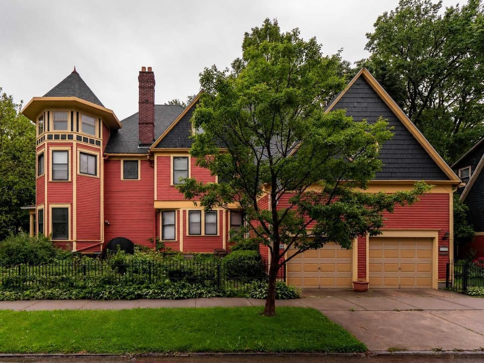 Classic facade w/ warm brick tones & inviting front porch framed by greenery.
