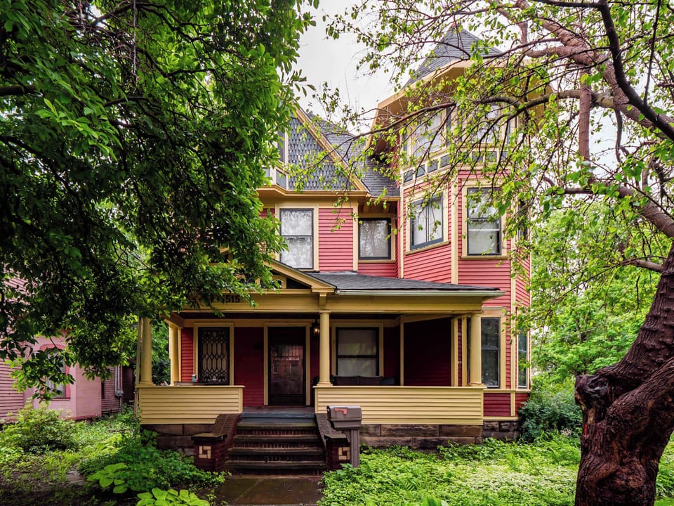 Charming red Victorian nestled among mature trees on a quiet, picturesque street.

