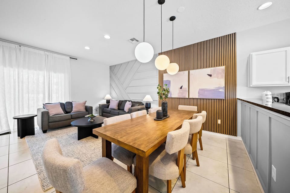Welcome to the stylish dining area with a rich wooden table and plush light-colored chairs, perfectly complementing the modern kitchen. Enjoy the cozy ambiance and soft lighting, perfect for meals and gatherings with loved ones.