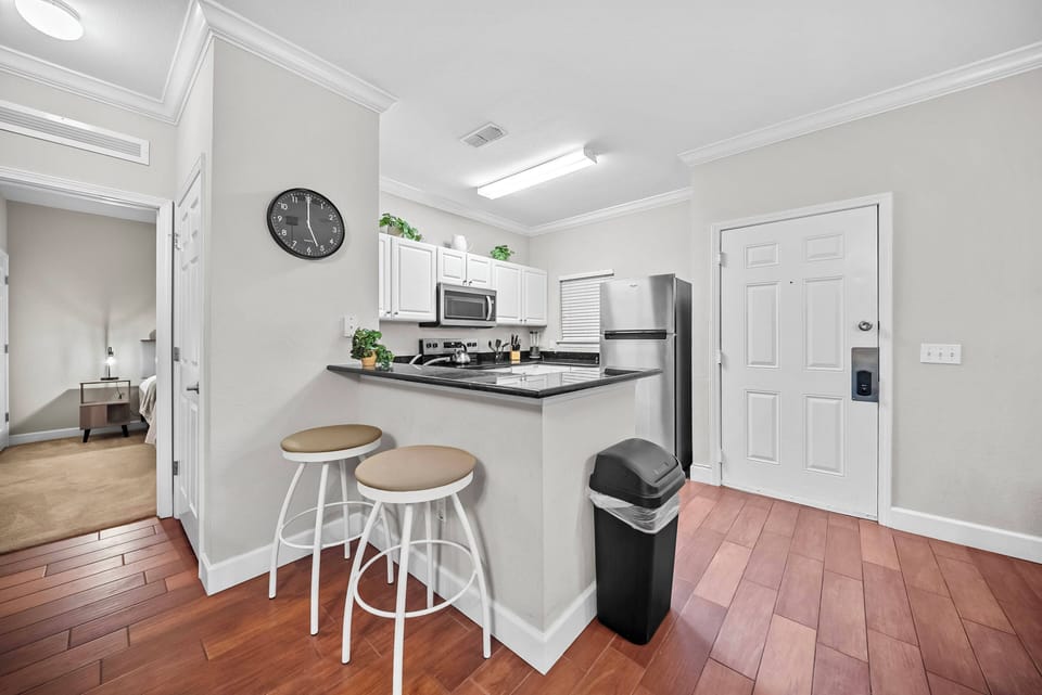 Welcome to this stylish kitchen featuring white cabinetry and warm wood flooring. The sleek bar area with modern stools is ideal for casual dining and conversation, all enhanced by natural light that creates a welcoming.