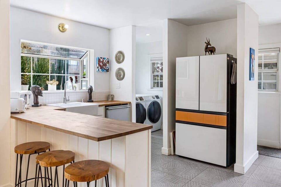 Bright kitchen featuring a modern French door refrigerator, butcher block island with bar seating, and an in-unit washer/dryer — everything you need for a comfortable stay