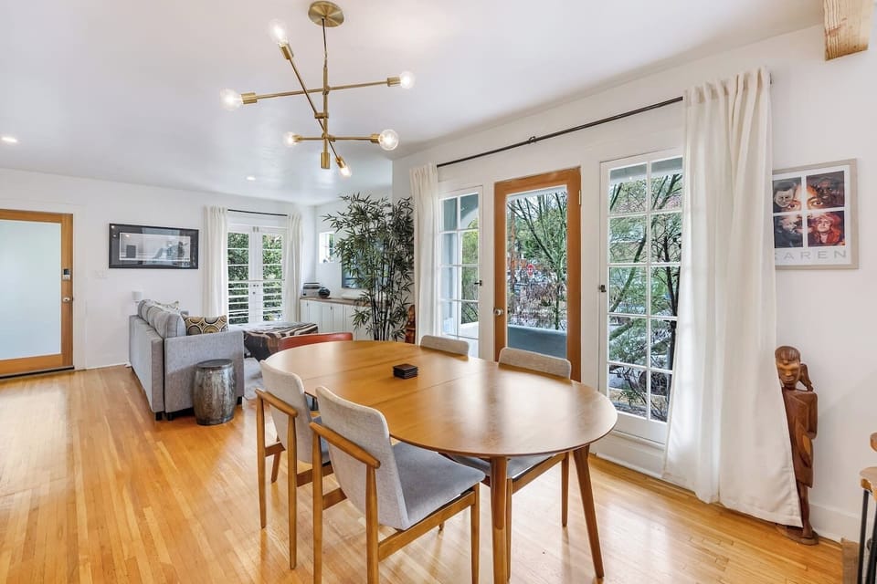 Sun-soaked dining area with a mid-century wood table, statement Sputnik chandelier, and French doors that open to the garden — meals here feel special