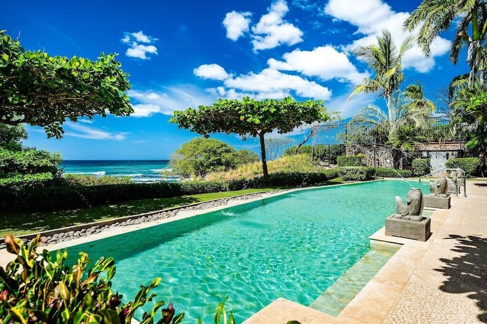Beachfront pool with tropical garden and direct beach access gate at luxury Playa Langosta condo, Tamarindo, Costa Rica. Ocean views, pool lounge area, sun loungers, and steps from surf, restaurants, shops, and premium vacation rentals.