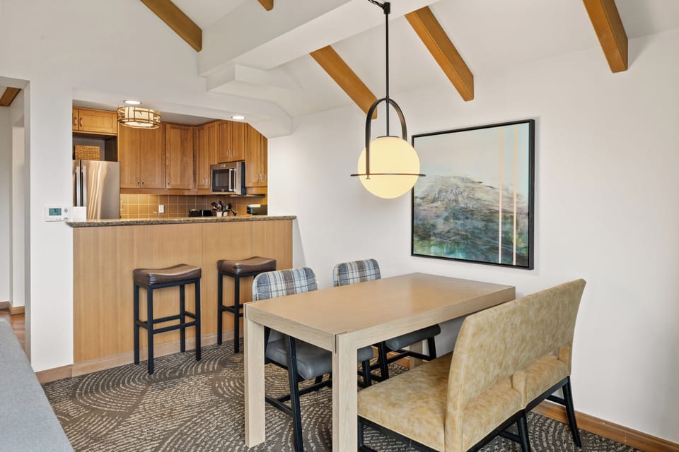 
Open-plan dining space seats 4–6 with a modern pendant light and exposed beam ceiling, steps from the fully equipped kitchen with bar seating.