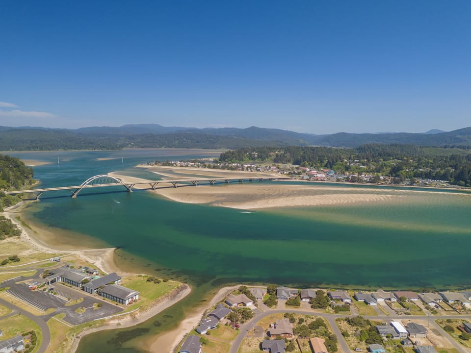 Aerial view showcasing the property's scenic waterfront location near a graceful bridge, surrounded by forested mountains and turquoise bay waters.