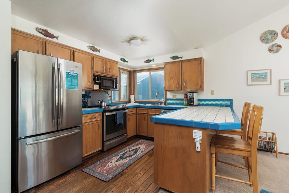 Your fully equipped kitchen features bright tile countertops, stainless steel appliances, and cheerful coastal touches. Warm wood cabinetry and natural light from the windows create a welcoming space to prepare meals together.