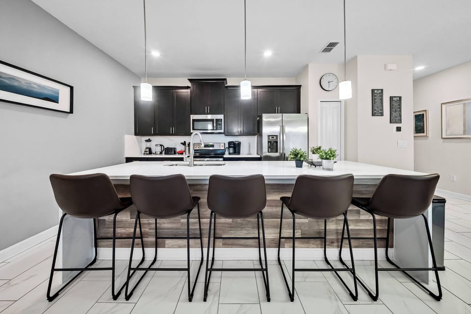 Enjoy delightful meals in this chic kitchen with elegant dark cabinetry and a spacious island. Modern bar stools are perfect for casual gatherings, and the bright lighting sets an inviting mood for cooking and conversation.
