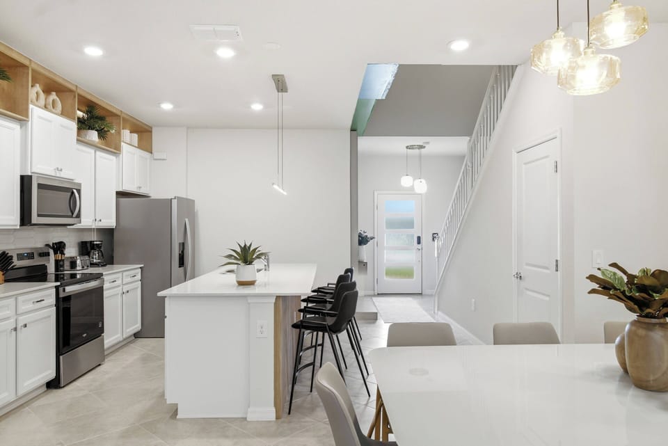 This bright kitchen boasts stylish white cabinetry and stainless steel appliances for a clean, functional space. The spacious island is ideal for casual dining and conversation, enhanced by warm, modern pendant lights.
