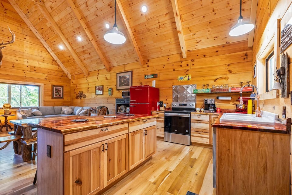 Open kitchen with polished wood floors, live-edge island, red retro refrigerator, and copper faucet by window.