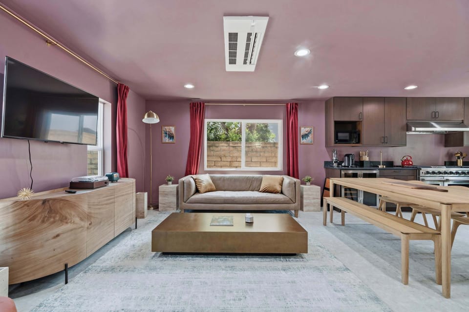 Open Plan Living and Dining — Large TV, Tan Sofa, Gold Coffee Table & Wood Dining Table Open to Kitchen