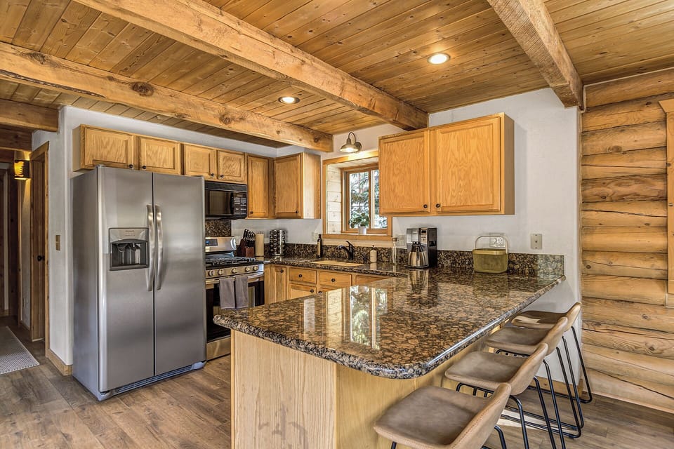 Cook and gather with ease in this warm cabin kitchen featuring granite countertops, stainless steel appliances, and bar seating.