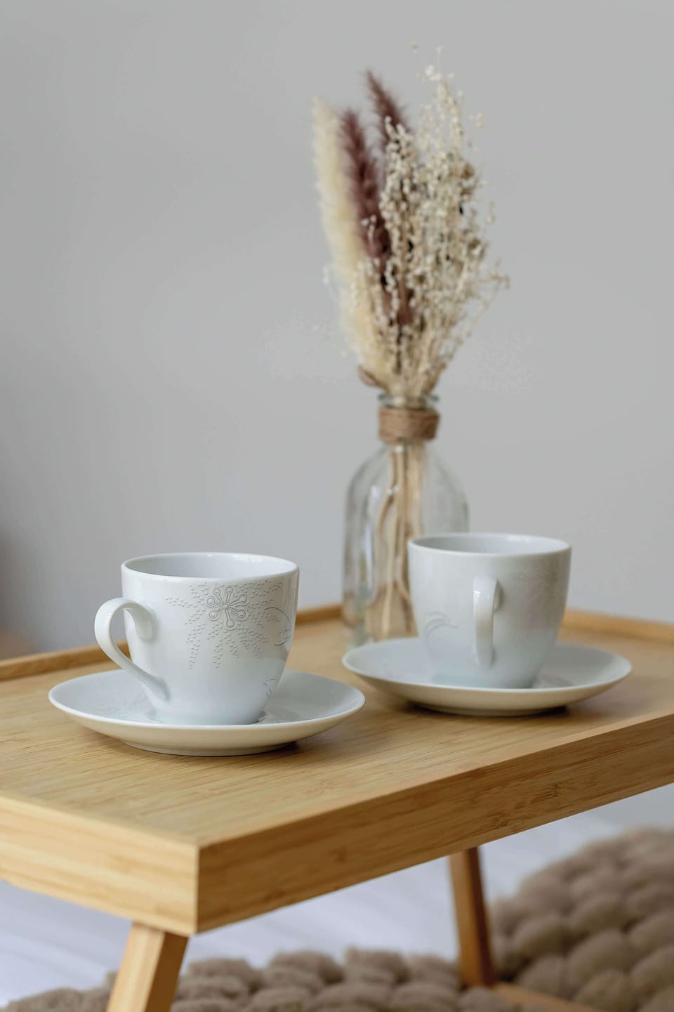 A small breakfast setup with cups of coffee and dried flowers on a wooden table.