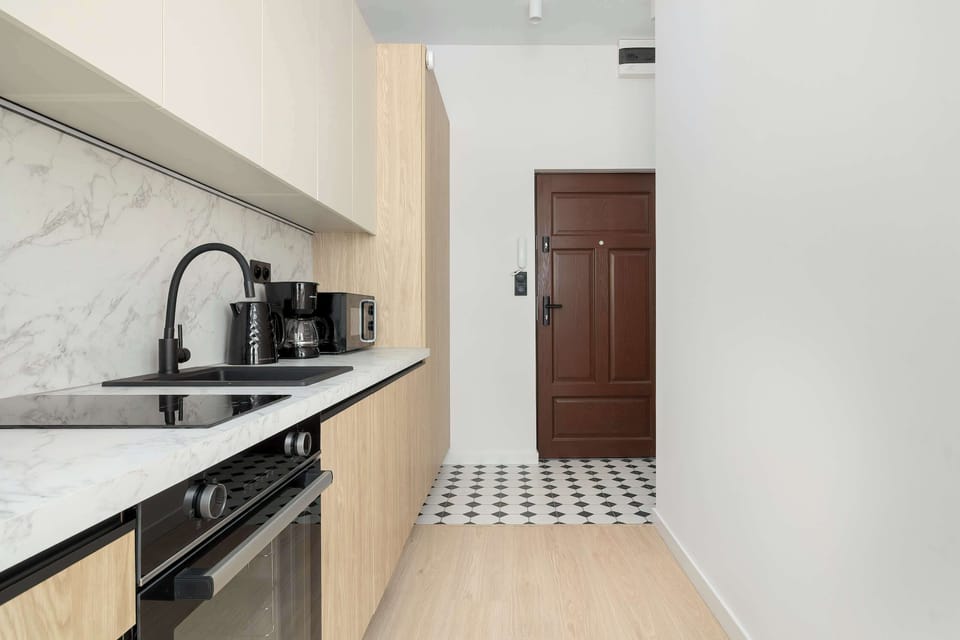 A hallway view of the kitchenette leading to the apartment entrance, designed in a clean contemporary style.