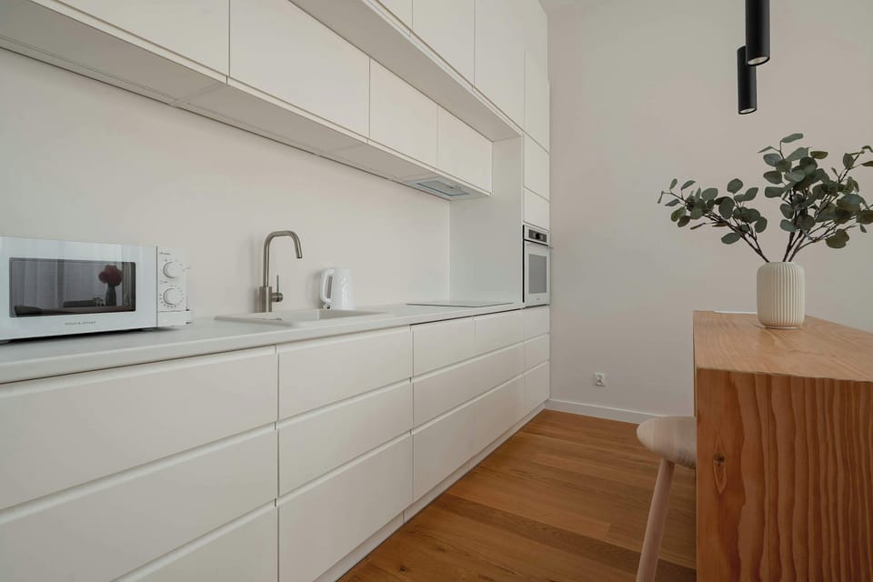 A long, modern kitchen with white cabinets, built-in appliances, and a clean countertop. The layout is designed for convenience and efficiency.