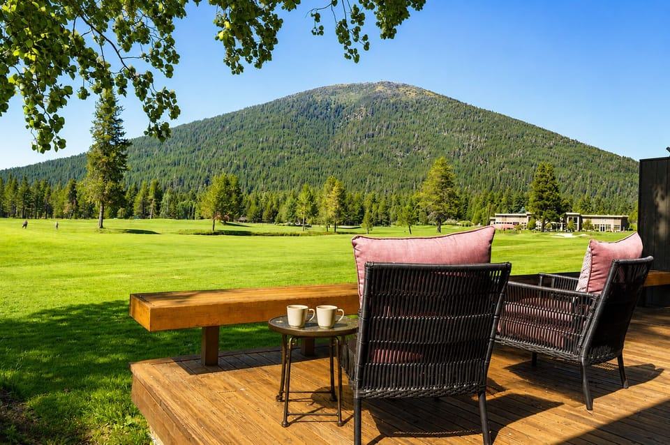 Expansive mountain views with forested slopes frame this serene outdoor setting, surrounded by open lawns and distant property buildings under clear blue skies.