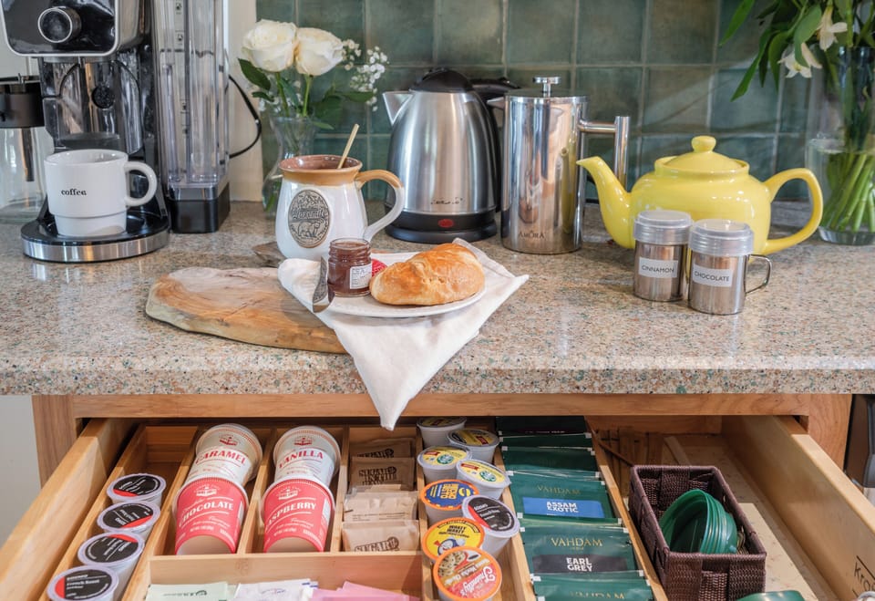 Stocked coffee and tea bar with K-cups, premium teas, hot chocolate, espresso machine, French press, and electric kettle—your morning ritual, fully covered.