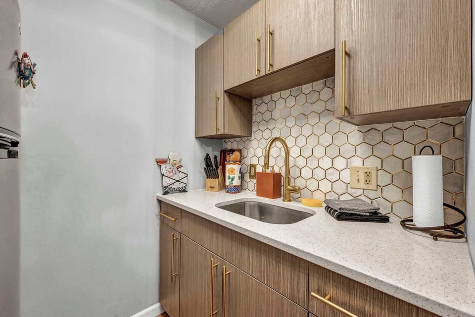 Kitchen w/ wood cabinetry, hexagon tile backsplash & sink.