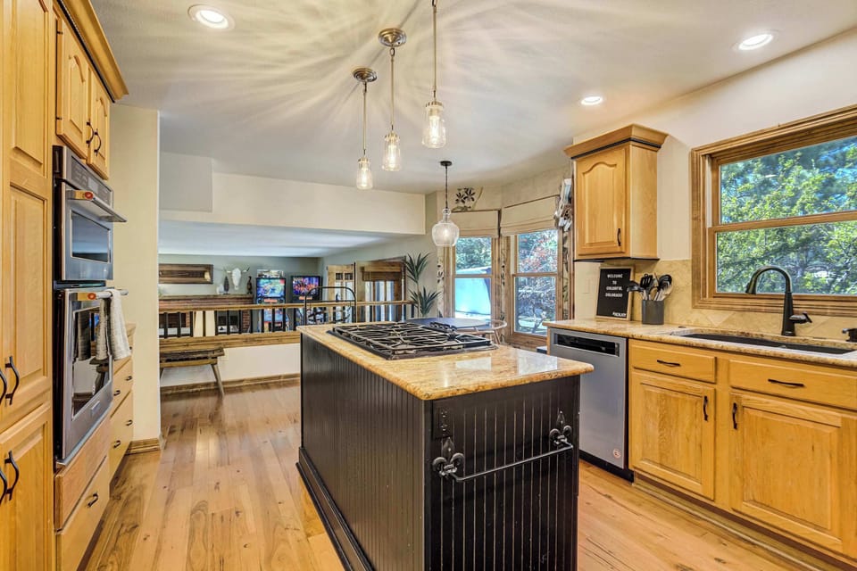 The full kitchen layout stretches from the central island with gas cooktop to the professional-grade appliances along the far wall, with pendant lighting overhead, granite countertops throughout, and the dining nook visible just beyond.