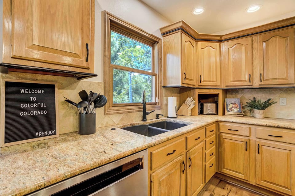 Warm wood cabinetry, granite countertops, and a undermount sink anchor this end of the kitchen, with a window above bringing in natural light and open shelving adding a warm, lived-in detail to the space.

