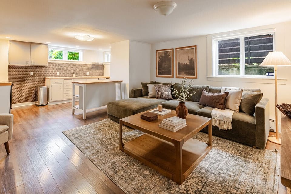Downstairs second living room with olive sectional, kitchenette, and warm artwork gallery wall