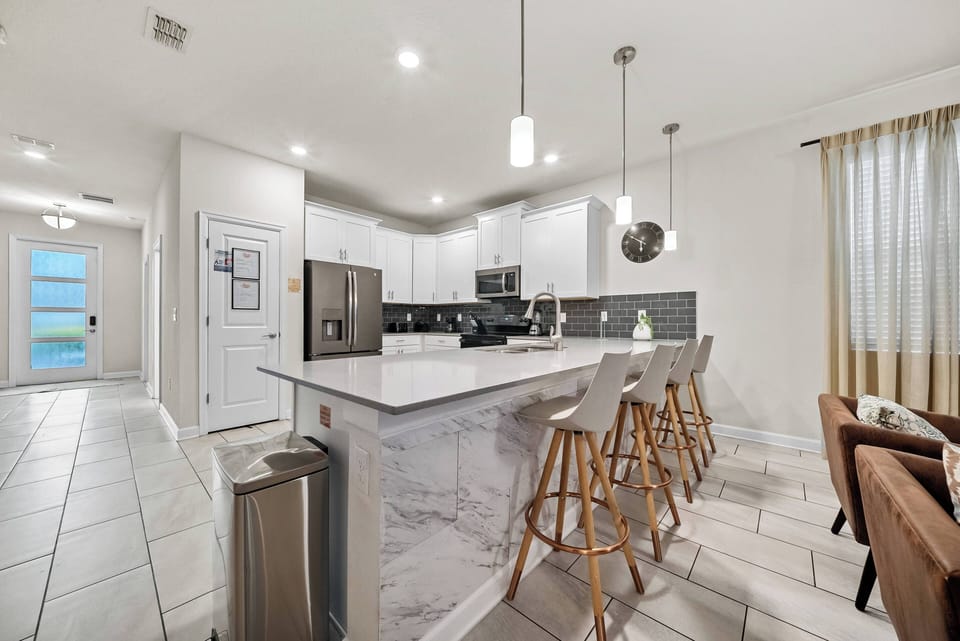 Discover a bright, airy kitchen with sleek white cabinetry and elegant marble countertops. Enjoy morning coffee at the inviting bar stools, and let the stylish lighting create a warm ambiance for your culinary adventures.