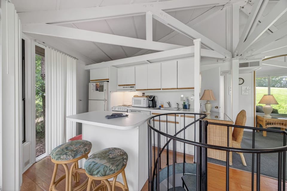 Your bright, airy kitchen awaits, featuring a spacious island for meal prep, white cabinetry, and modern appliances. The vaulted ceiling with exposed beams adds charm, while natural light streams in.