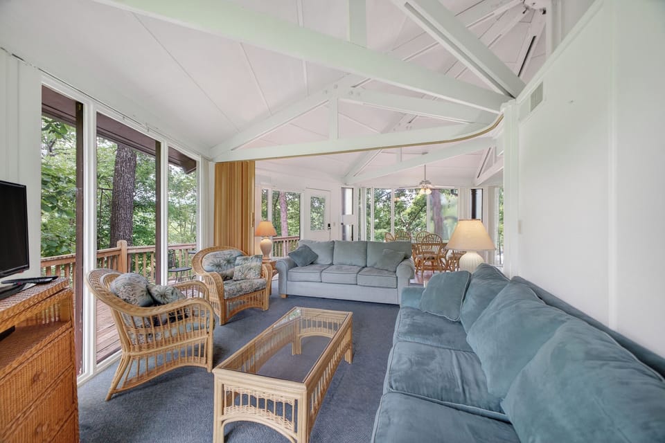 Unwind in your light-filled living room, where floor-to-ceiling windows frame lush forest views and cozy coastal furniture invites you to relax after a day of exploration.