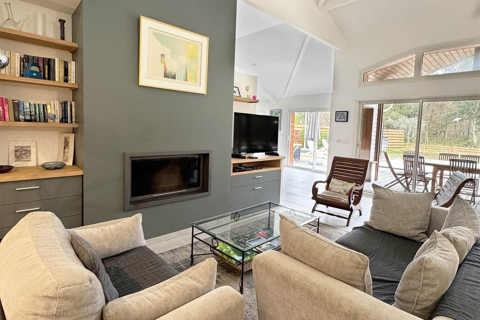 Living room, fireplace, grey sofas, high ceilings, large windows, natural light:<br>The spacious living room features high ceilings, a fireplace, and generous natural light — a refined space to unwind after a day at the beach or on the golf course.