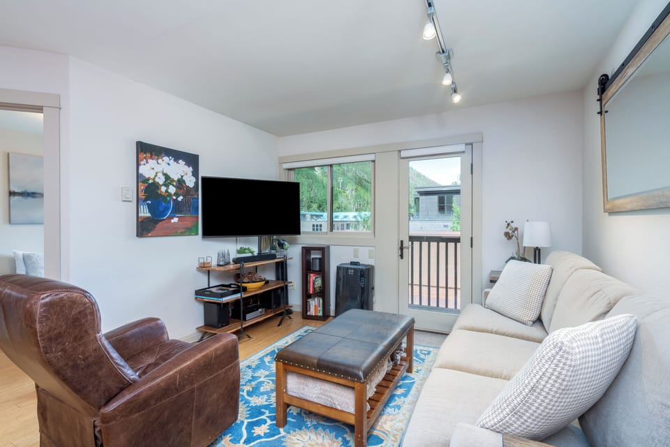 Relax in your bright, welcoming living room with plush seating, track lighting, and doors opening to your private balcony with mountain views.