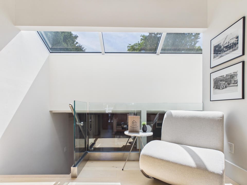 A cozy upper-level landing featuring a plush lounge chair, marble accents, and an architectural glass railing overlooking the sunlit spaces below.