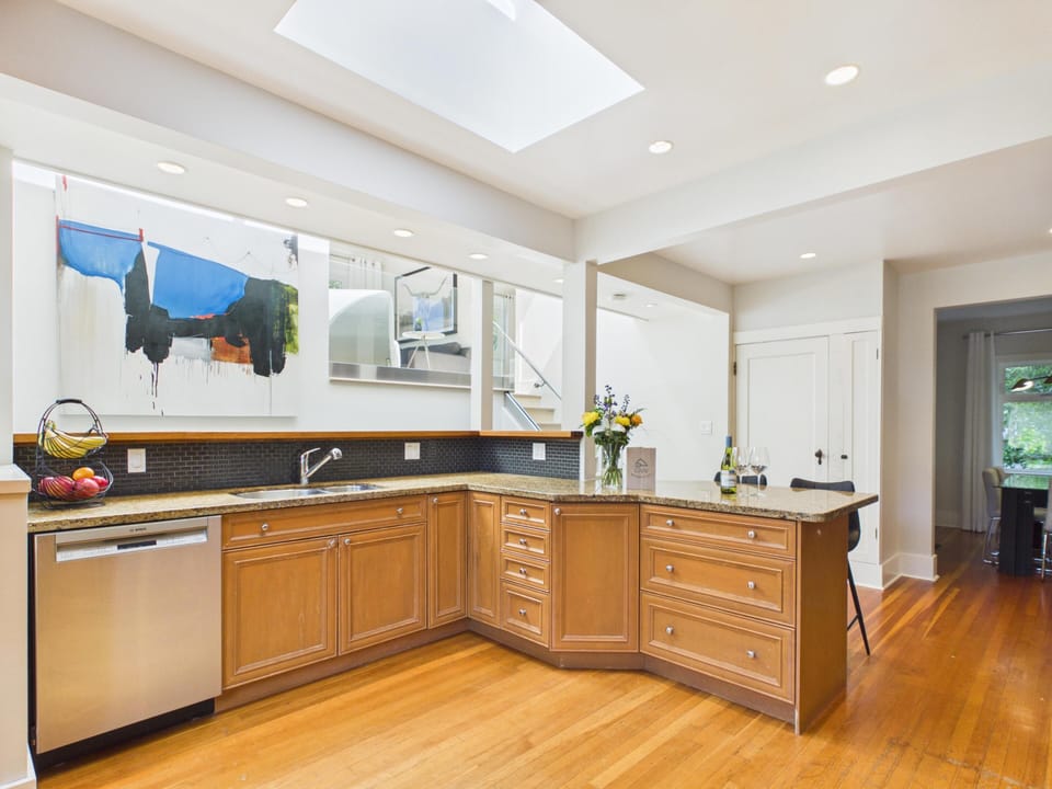 The heart of the home! This gorgeous kitchen features rich honey-wood cabinetry, premium granite countertops, a sleek black tile backsplash, and a massive overhead skylight that floods the space with sunshine.