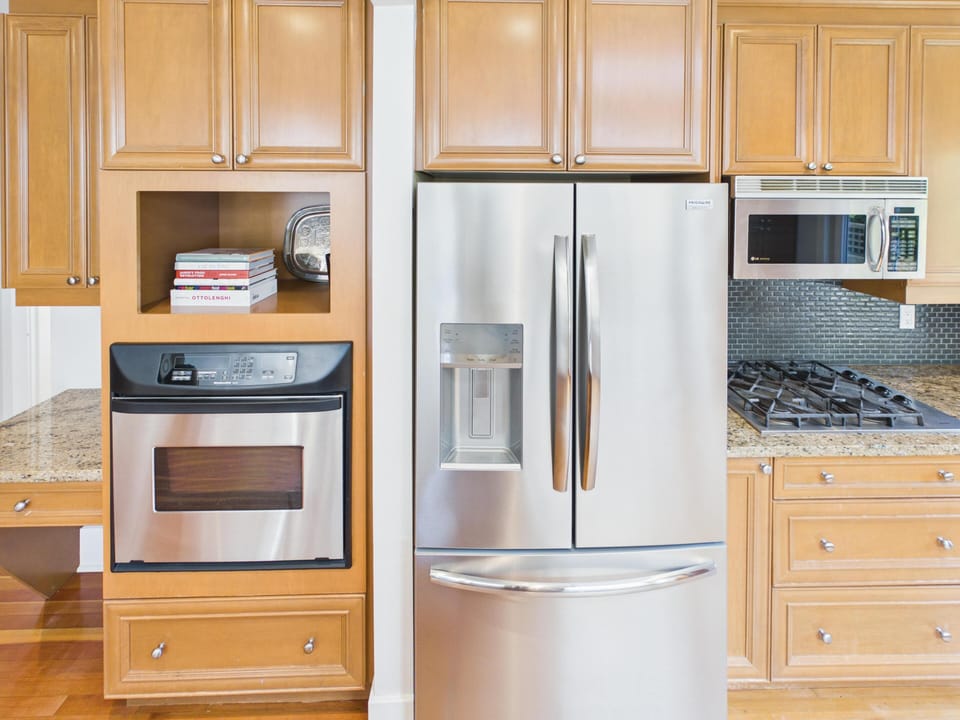 A closer look at the gourmet setup, featuring a built-in microwave, an expansive French-door refrigerator, and beautiful custom woodwork.