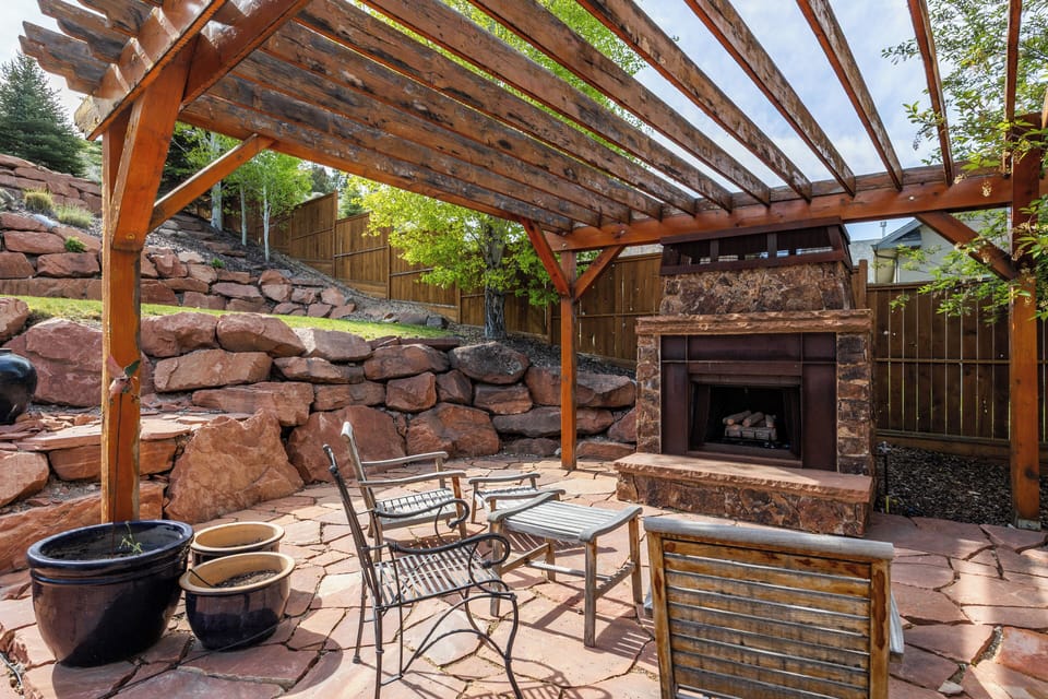 Charming outdoor patio featuring a stone fireplace, pergola seating area, and a cozy setting for relaxing evenings outdoors.