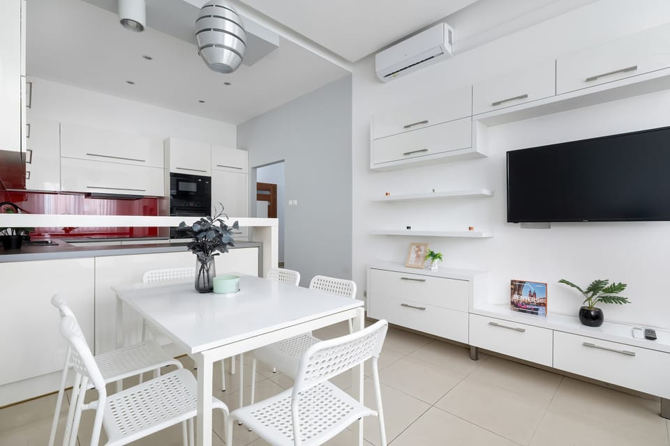 A stylish open-plan kitchen and dining area with white cabinets and red wall panels. The glossy surfaces and modern finishes add a luxurious touch.