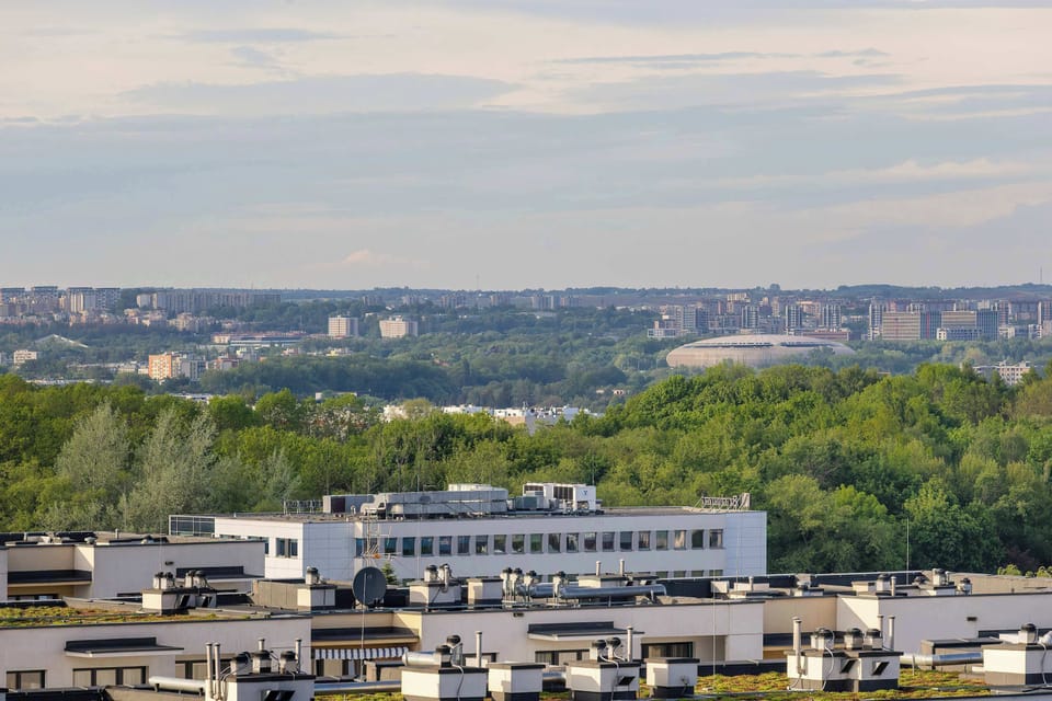 A wide landscape view featuring apartment blocks, treetops, and open sky stretching across the horizon. Natural greenery contrasts beautifully with the city architecture.