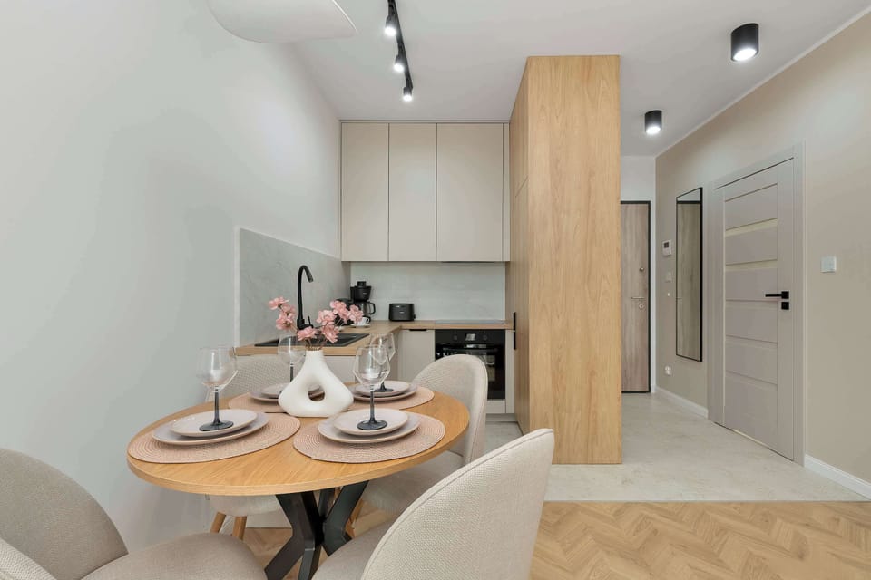 A perspective view from the living room looking through an open white door into the elegant bedroom. The light wooden flooring and neutral color palette create a continuous and harmonious flow between the rooms.