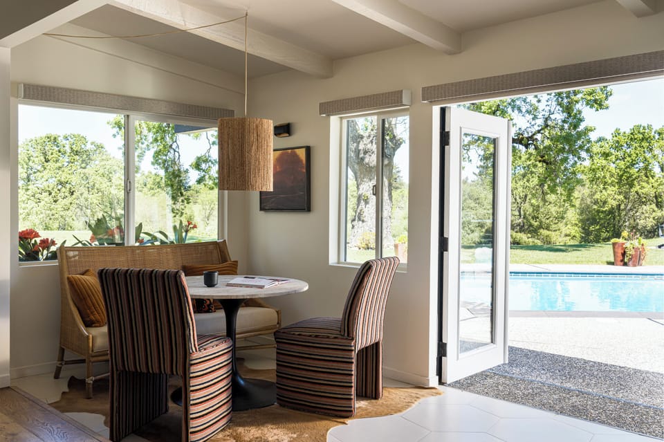 Enjoy your morning coffee at this inviting dining nook, where large windows frame serene pool and garden views, creating your perfect breakfast retreat.