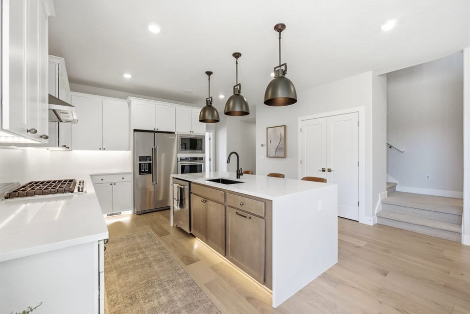 Bright modern kitchen with white cabinetry, stainless steel appliances, large island, and warm wood accents.
