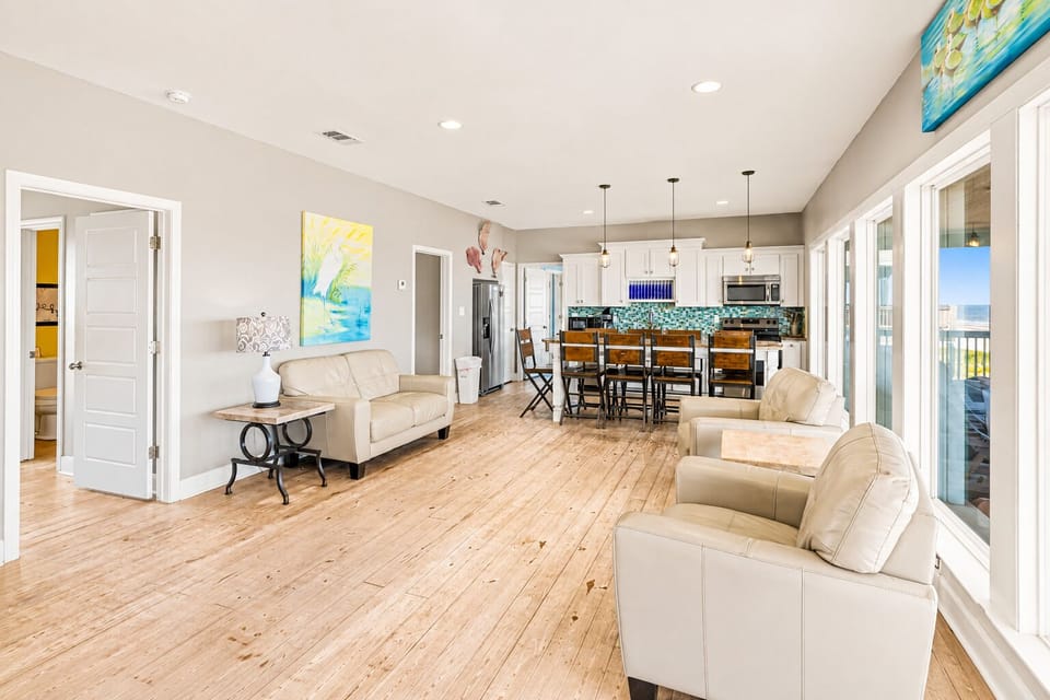 Spacious open living area with recliners, sofa seating, dining table and kitchen in the background, plus bright natural light from Gulf-facing windows.