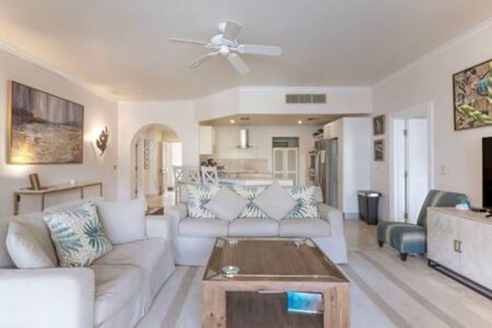 Light and airy living area with comfortable seating and flat screen TV and a ceiling fan for cooling.