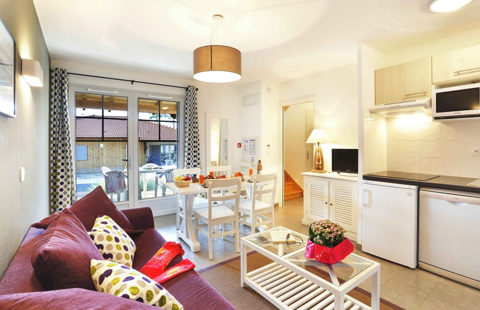 Open-plan lounge with purple sofa and dining area — the sofa converts to a double bed for two additional guests.