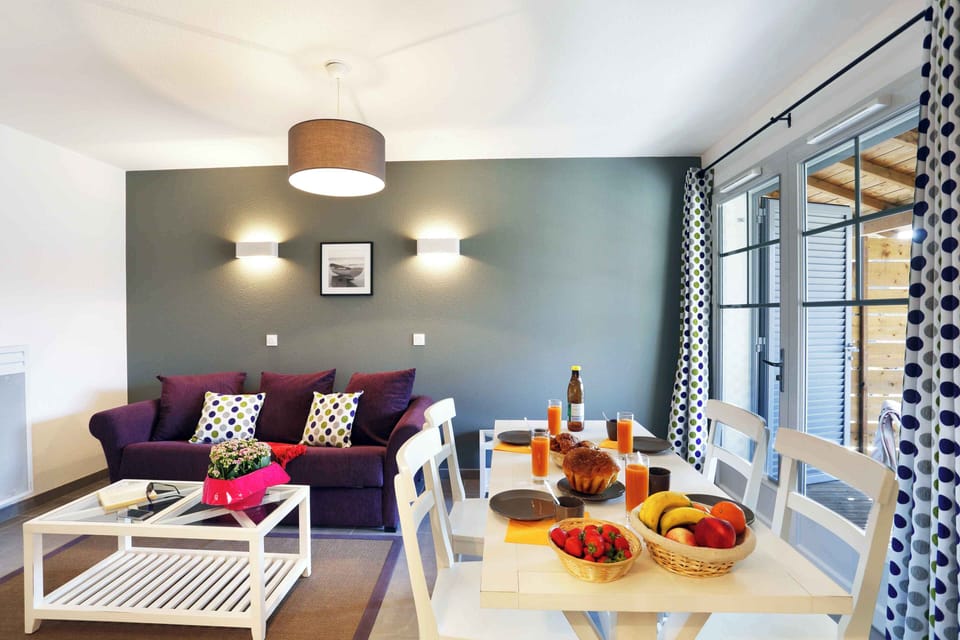 Living area from the kitchen side — pine forest visible through the glass doors leading to the furnished terrace.