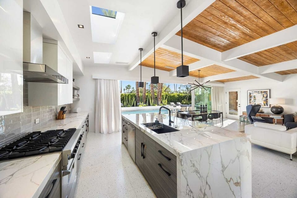 Chef's kitchen with marble surfaces, a professional six-burner range, and unobstructed views to the pool.