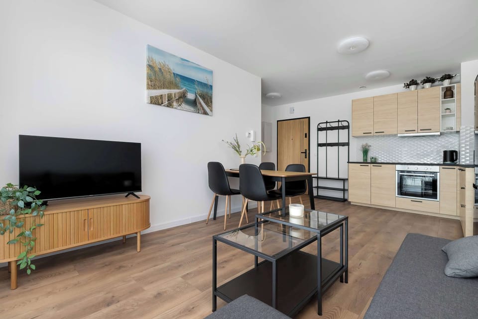 A view of the living room looking towards the kitchen, showing a flat-screen TV on a wooden console. A glass coffee table sits on the laminate flooring in the center.