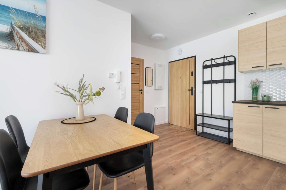 A dining area within the apartment featuring a wooden table surrounded by stylish black chairs. In the background, an open hallway and kitchen cabinets are visible.